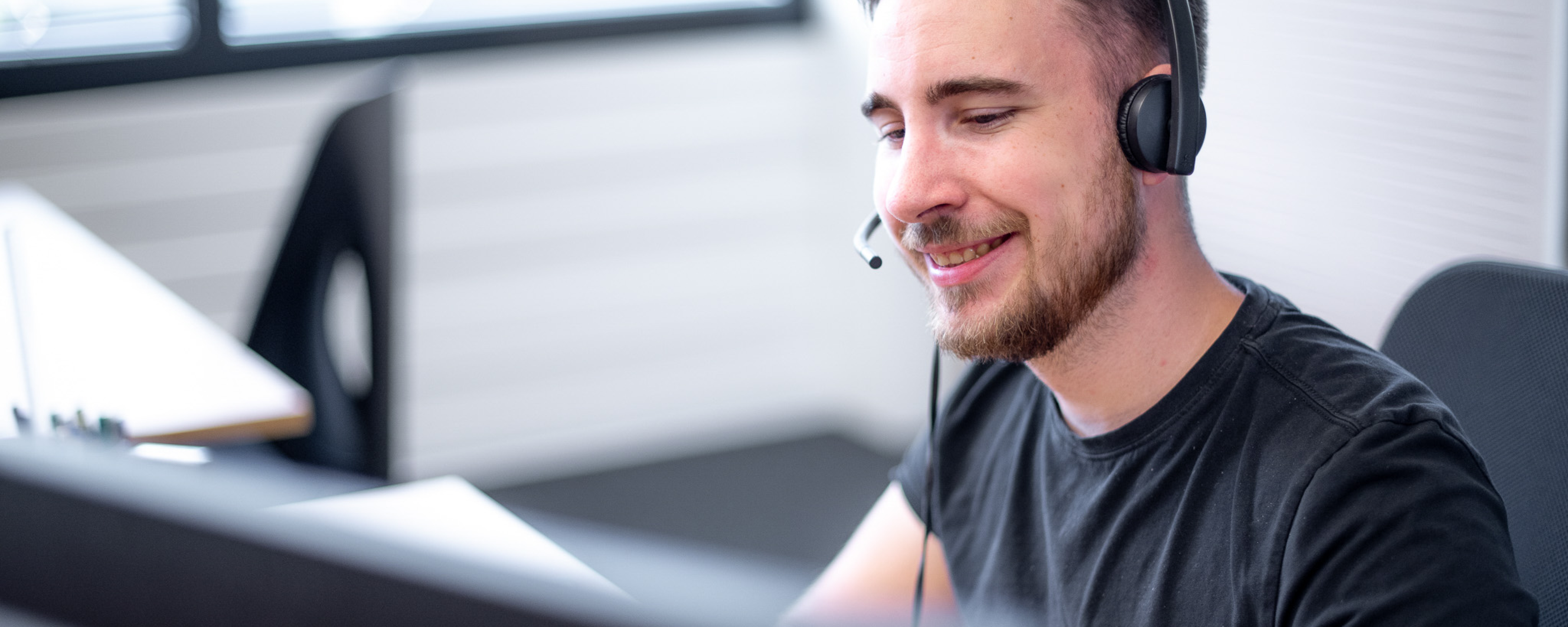 Employee smiling with headset on in front of computer