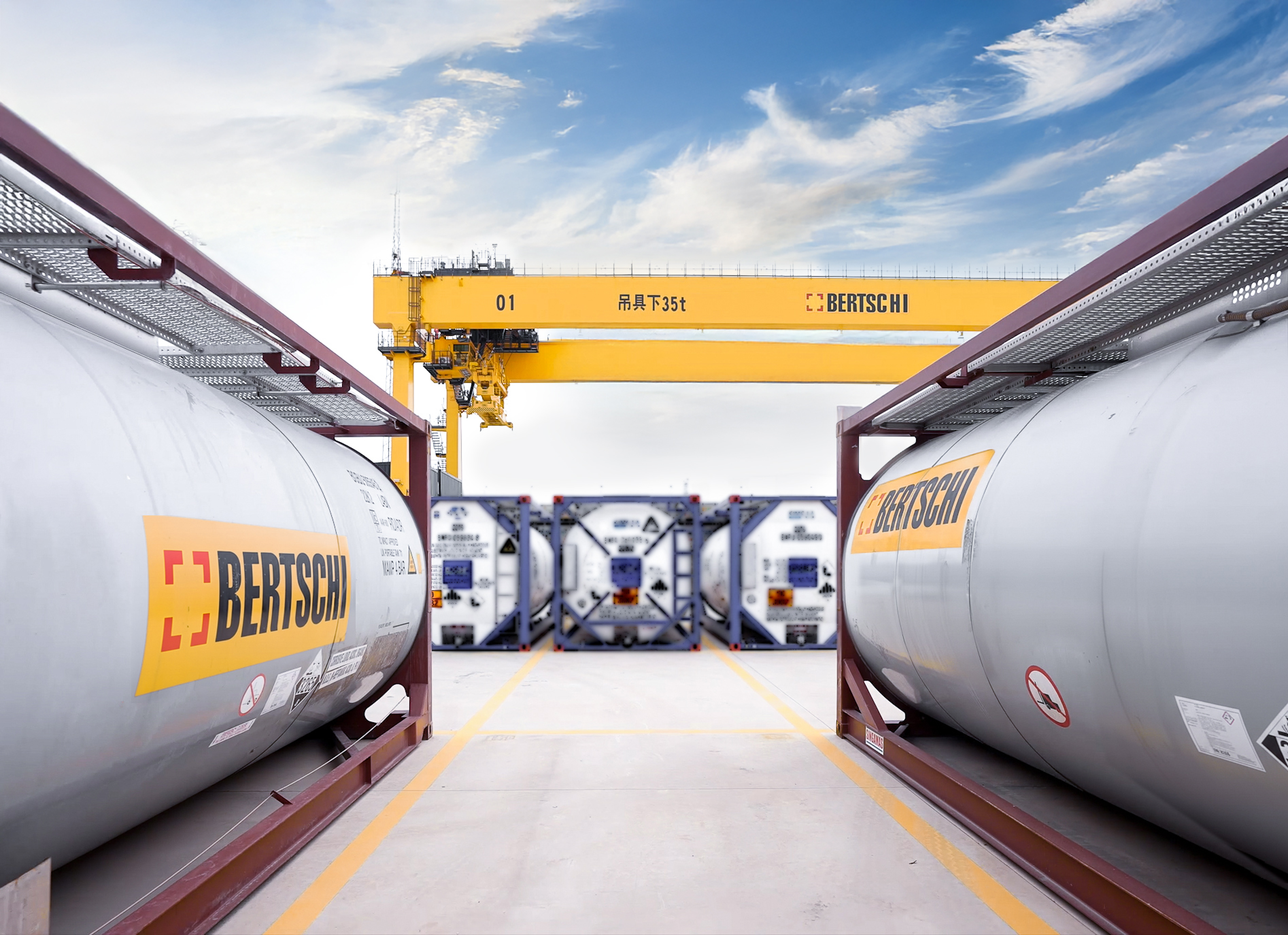 two bertschi isotanks facing a big yellow gantry crane