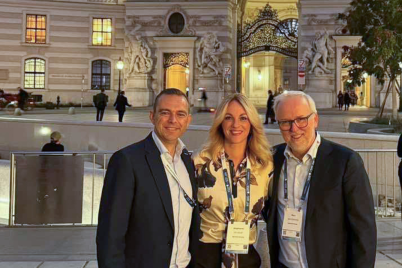 Three conference attendees pose outside an illuminated historic building in Vienna.